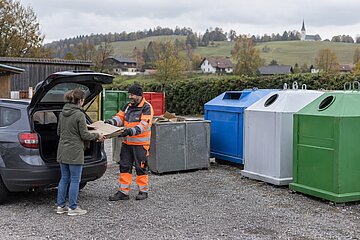 Wertstoffsammelzentrum mit Containern, ein Mitarbeiter hilft beim Abladen
